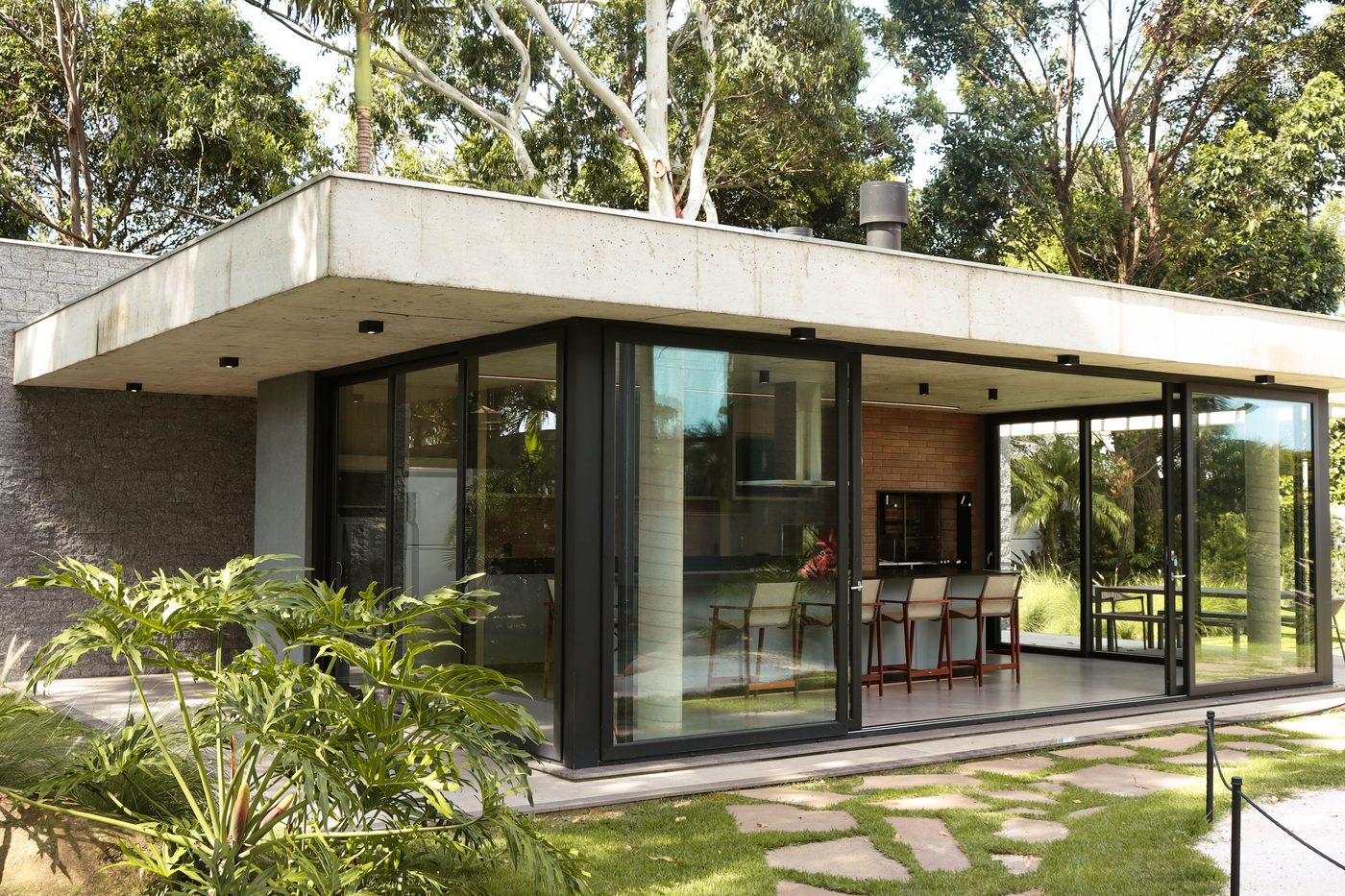 Pavilhão gourmet de vidro e concreto, cercado de mata