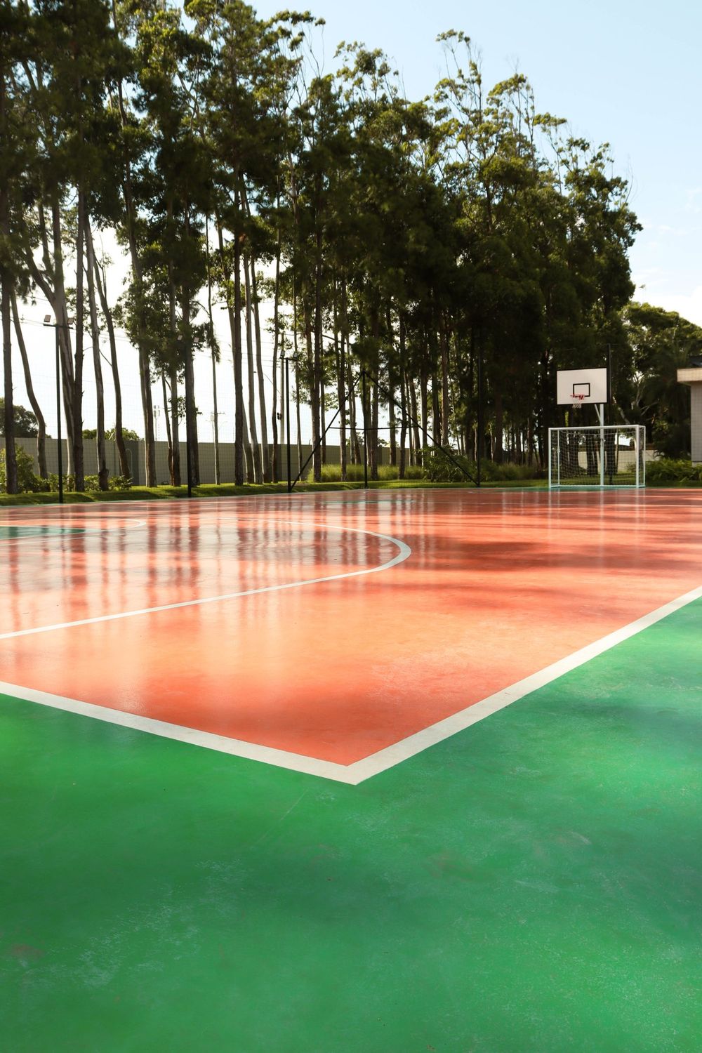 Quadra poliesportiva com cesta de basquete, cercada de árvores
