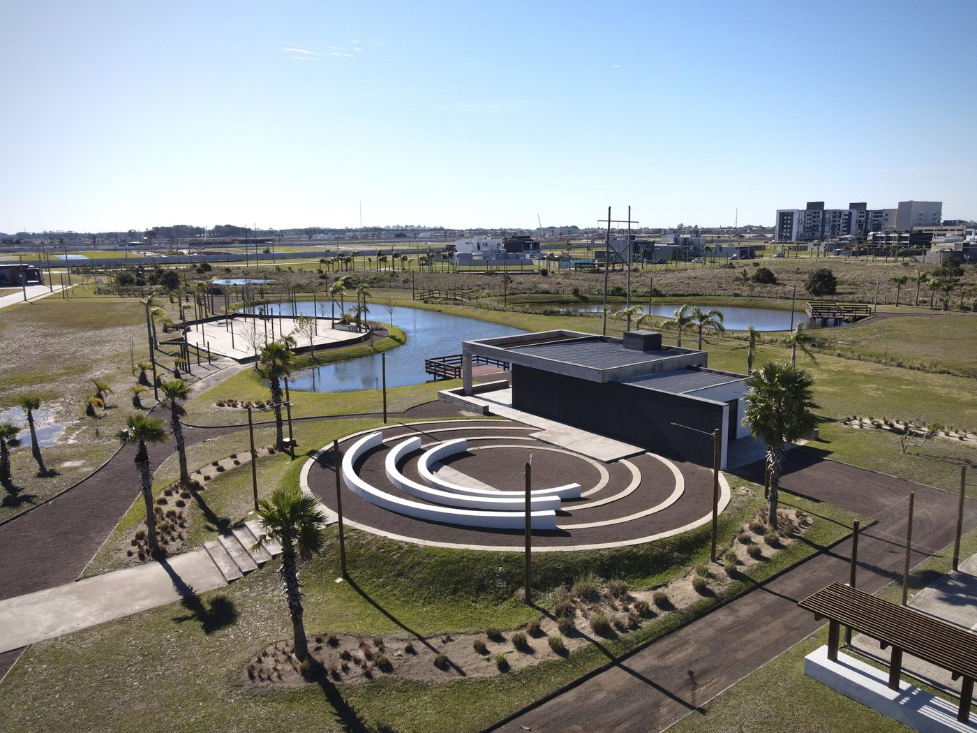 Anfiteatro de concreto com arquibancada circular, palmeiras e lago ao lado