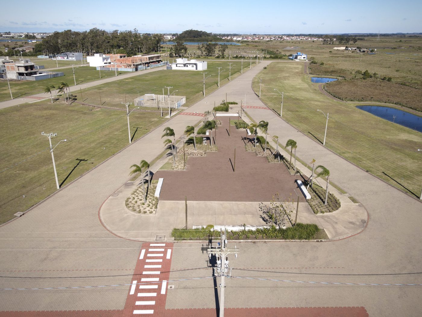 Avenida pavimentada com praça central arborizada e faixa de pedestre