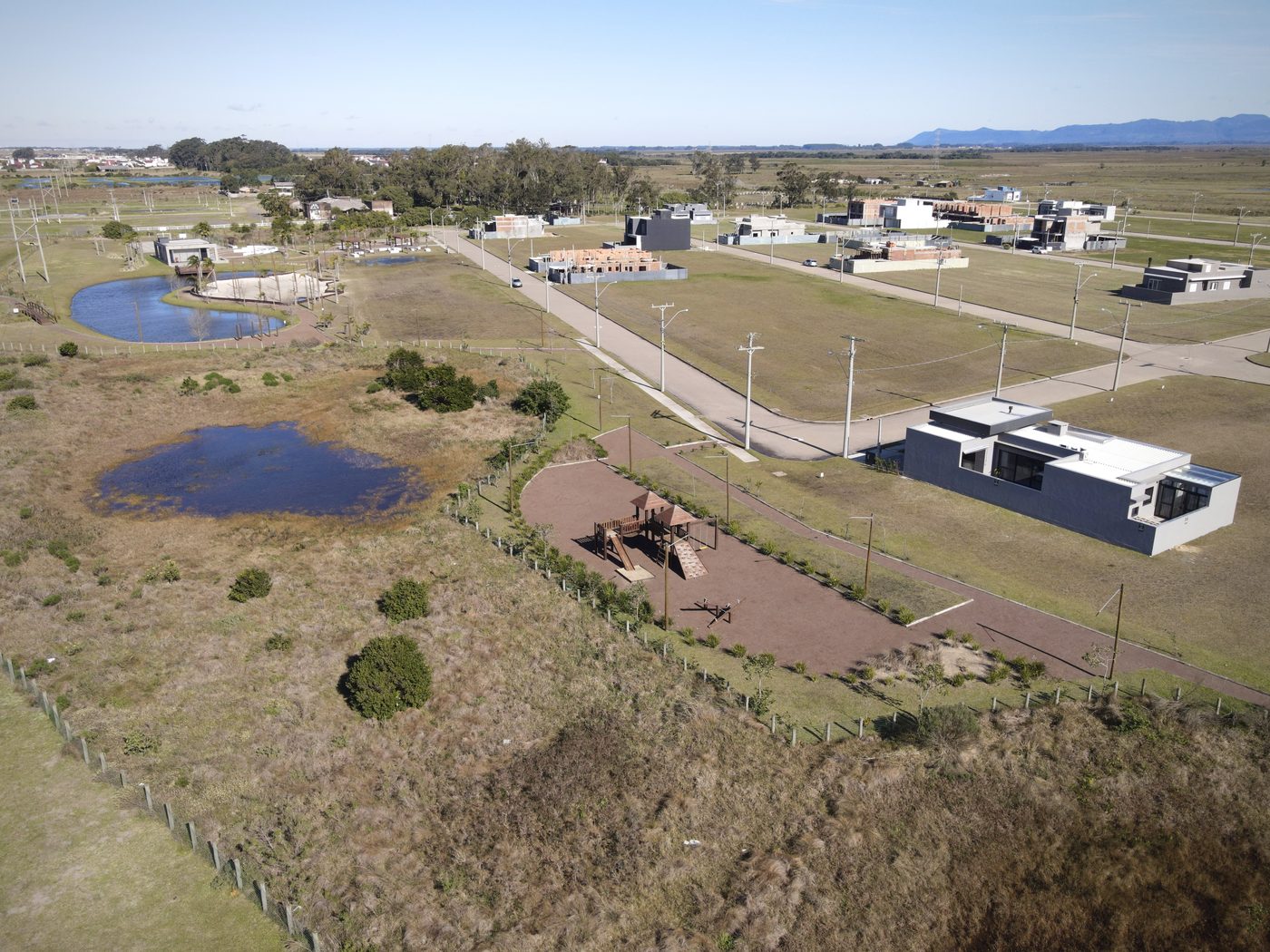 Rua do bairro com casas construídas e outras em obra, playground e lago