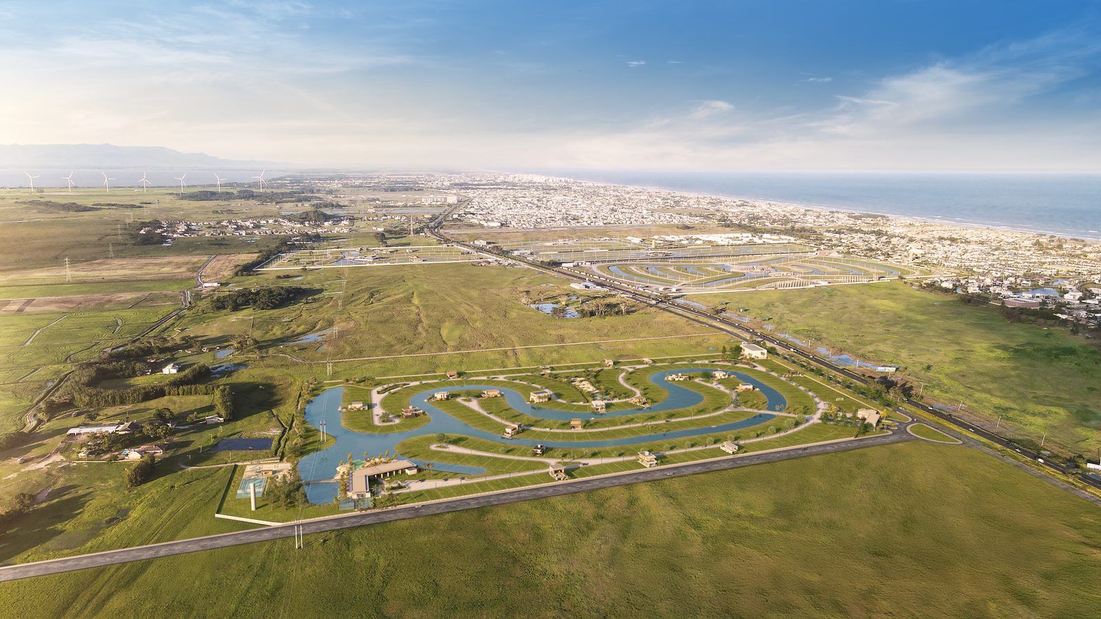 Vista aérea do condomínio inteiro, com o lago serpenteando entre os lotes e o mar ao fundo